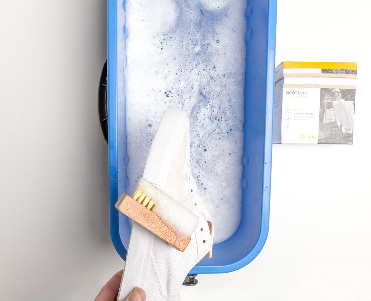 White Collective Canvas Sneakers being held above soapy water in a blue bucket.