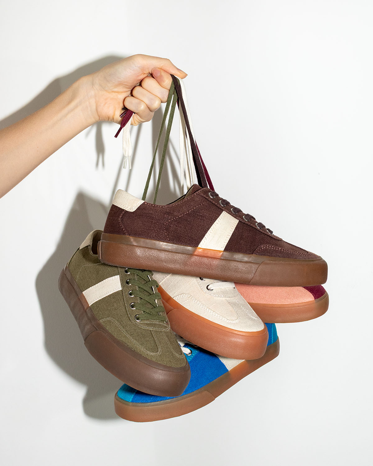 A hand holding five pairs of hemp sneakers by their laces